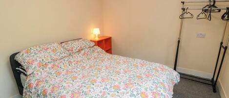 A bedroom with a floral bedspread, a bedside table with a lamp, and a clothing rack.