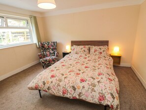A bedroom with a floral bedspread, a chair, two bedside lamps, and a window with curtains. - Grove Stables House (Yarm)