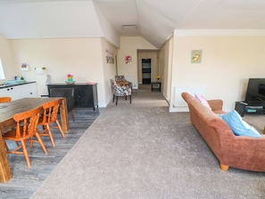 Un salon avec un canapé, une table à manger et des chaises, un coin cuisine et un couloir menant à une autre pièce.