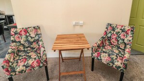 A room with a wooden table and two floral armchairs, a painting of a beach on the wall, and a green door. - Grove Stables House (Yarm)