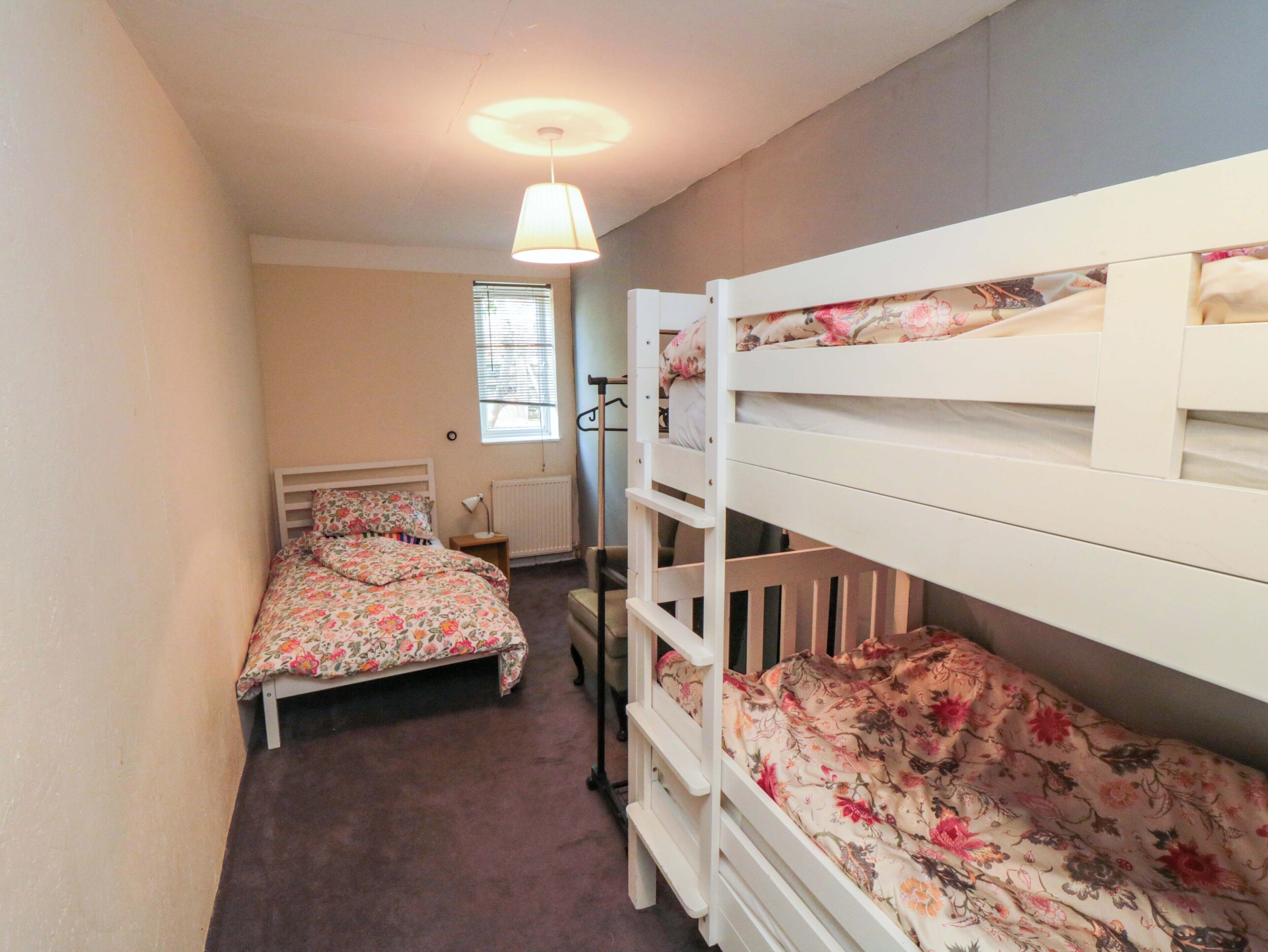 Un dormitorio con dos literas, una ventana con persianas, un radiador y una lámpara colgante.