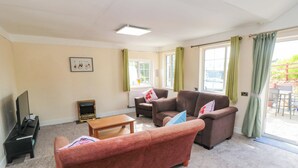 A living room with a sofa, armchairs, a coffee table, a TV, and a fireplace. - Grove Stables House (Yarm)