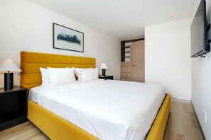 Ein modernes Hotelzimmer mit einem großen Bett, zwei Nachttischen, einem Wand-Fernseher und einem Holzschrank.