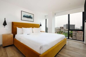 Ein modernes Hotelzimmer mit einem großen Bett, Blick auf die Stadt und einem gerahmten Kunstwerk an der Wand.
