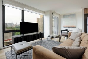 Ein modernes Wohnzimmer mit einem großen Fenster, einem Flachbildfernseher, einer Couch und einem kleinen Tisch.