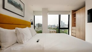 A modern hotel room with a large bed, a view of the city, and a wooden wardrobe. - w Amazing 2BR w/ AC in the Heart of Cuauhtémoc (Mexico City)