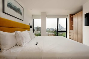 Ein modernes Hotelzimmer mit einem großen Bett, Blick auf die Stadt und einem Holzschrank.
