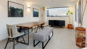 Ein moderner Essbereich mit einem Holztisch, einer Bank und Blick auf die Stadt durch große Fenster.