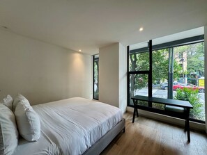 Ein modernes Schlafzimmer mit einem großen Fenster, einem Bett mit weißer Bettwäsche und einer Bank am Fenster.