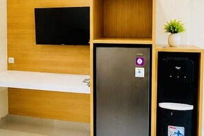 Une chambre moderne dotée d’un téléviseur à écran plat fixé au mur, d’un réfrigérateur intégré et d’un distributeur d’eau.