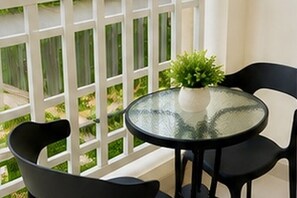 Un balcon avec une table en verre et deux chaises, un pot de fleurs et une rambarde blanche.