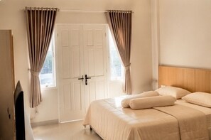 Une chambre à coucher avec un lit, des rideaux, une porte et un téléviseur.