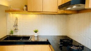 A modern kitchen with wooden cabinets, a black countertop, a gas stove, and a white tiled backsplash. - Elimstay Hospitality Jimbaran Bali | Comfort, Pool & Tropical Ambience (Badung)