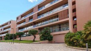 Un hotel de varios pisos con balcones, un camino de entrada pavimentado y vegetación ajardinada.
