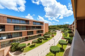 Um edifício moderno de vários andares, com varandas, um caminho pavimentado e áreas verdes bem cuidadas.