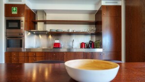 Una cocina moderna con microondas, horno y tostadora. En primer plano, una mesa de madera con un cuenco.