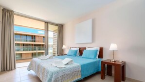 Habitación de hotel con cama, dos mesitas de noche, ventana con cortinas y vista a un edificio.