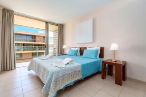 Quarto de hotel com cama, duas mesas de cabeceira, janela com cortinas e vista para um edifício.