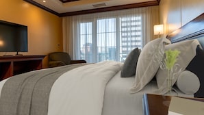 Una camera d'albergo con un letto grande, una televisione, una sedia e una finestra vista città.
