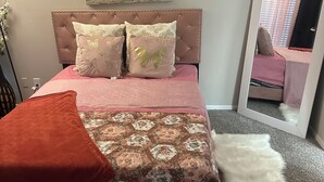 Quarto com cama, espelho, um objeto decorativo na parede e piso coberto por carpete.