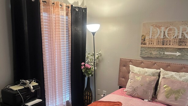 Um quarto com uma cama, uma escrivaninha com impressora, uma luminária e um cartaz na parede.