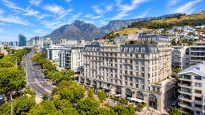 A cityscape with a prominent building featuring multiple floors and a central courtyard, surrounded by lush greenery and a mountain in the background. - Green Point Luxury Suite Pool + V&A Waterfront (Cape Town)