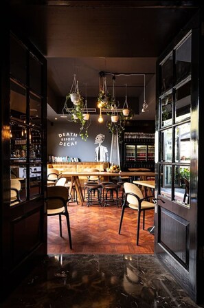 Ein gemütliches Café-Interieur mit einer Bar, Holztischen, Stühlen und hängenden Pflanzen.