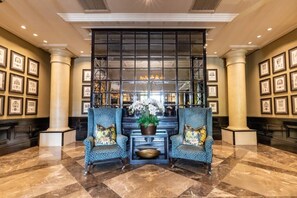Eine Lobby mit zwei gemusterten Sesseln, einem großen Fenster und gerahmten Bildern an den Wänden.