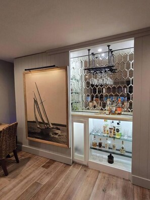 A bar area with a hexagonal patterned wall, a sailboat painting, and various bottles. - Annapolis Retreat | Outdoor Kitchen + Fire Pit (Annapolis)