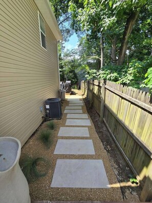 A narrow pathway leading to a house with a wooden fence and trees. - Annapolis Retreat | Outdoor Kitchen + Fire Pit (Annapolis)