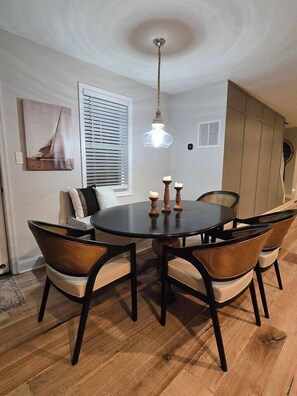 A dining area with a round table, four chairs, a ceiling light, and a window with blinds. - Annapolis Retreat | Outdoor Kitchen + Fire Pit (Annapolis)