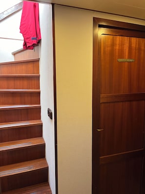 A wooden staircase leading to a door with a brass plate, a red jacket hanging on the wall, and a textured wall. - Beautiful accommodation in the center of Lübeck (Lübeck)