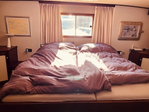 A bed with a blanket, a window with curtains, a wall with a framed picture, and a nightstand with a lamp. - Beautiful accommodation in the center of Lübeck (Lübeck)