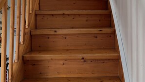 Una escalera de madera con barandilla, paredes blancas y un cuadro pequeño en la pared.