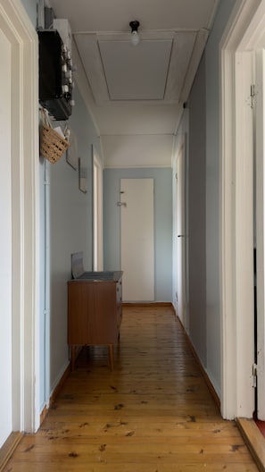 A hallway with wooden flooring, a dresser, a basket, and a white door at the end.