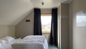 Un dormitorio con cama, ventana con cortinas, perchero y vista a edificios.