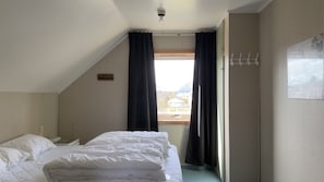 Um quarto com cama, janela com cortinas, um cabideiro e vista para edifícios.