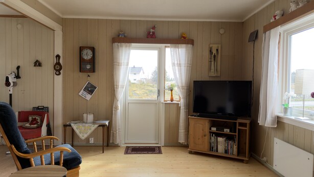 Una sala de estar acogedora con televisor, muebles de madera, un reloj y una ventana con cortinas.