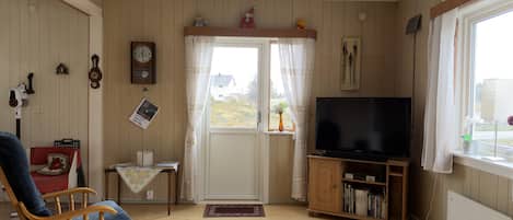 A cozy living room with a television, wooden furniture, a clock, and a window with curtains.