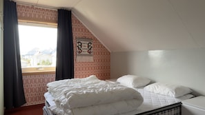 Quarto com cama, janela com cortinas, papel de parede estampado e um objeto pendurado na parede.