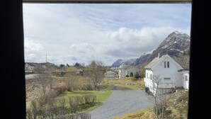Un paisaje rural con casas, un camino de grava y montañas al fondo.