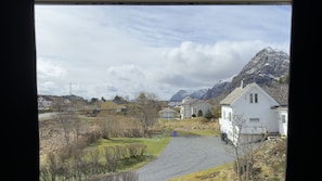 Un paisaje rural con casas, un camino de grava y montañas al fondo.