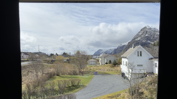 Paisagem rural com casas, um caminho de cascalho e montanhas ao fundo.