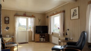Un salón acogedor con televisor, paredes de madera, estantería y una ventana con cortinas.