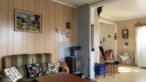 Una sala de estar acogedora con un panel de pared de madera, un cuadro, una chimenea, un sofá con cojines estampados y una mesa de comedor.