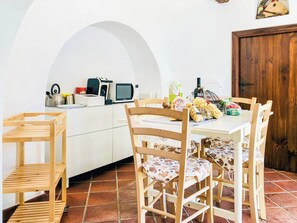 Ein Essbereich mit einem weißen Tisch, Holzstühlen, einem Fliesenboden und einer Küche im Hintergrund.