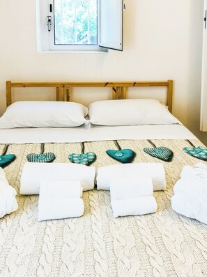 Ein Bett mit weißen Bettwäsche, einem hölzernen Kopfteil und herzförmigen Kissen.