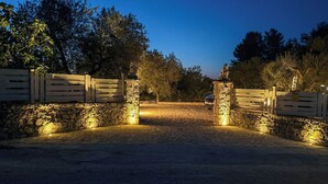 Une entrée fermée par un portail, avec des murs en pierre et un portail en bois, qui mène à une zone dallée.