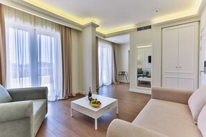 A modern living room with a sofa, a coffee table with fruit, and a view of a cityscape through large windows. - Hotel Eden (Budva)