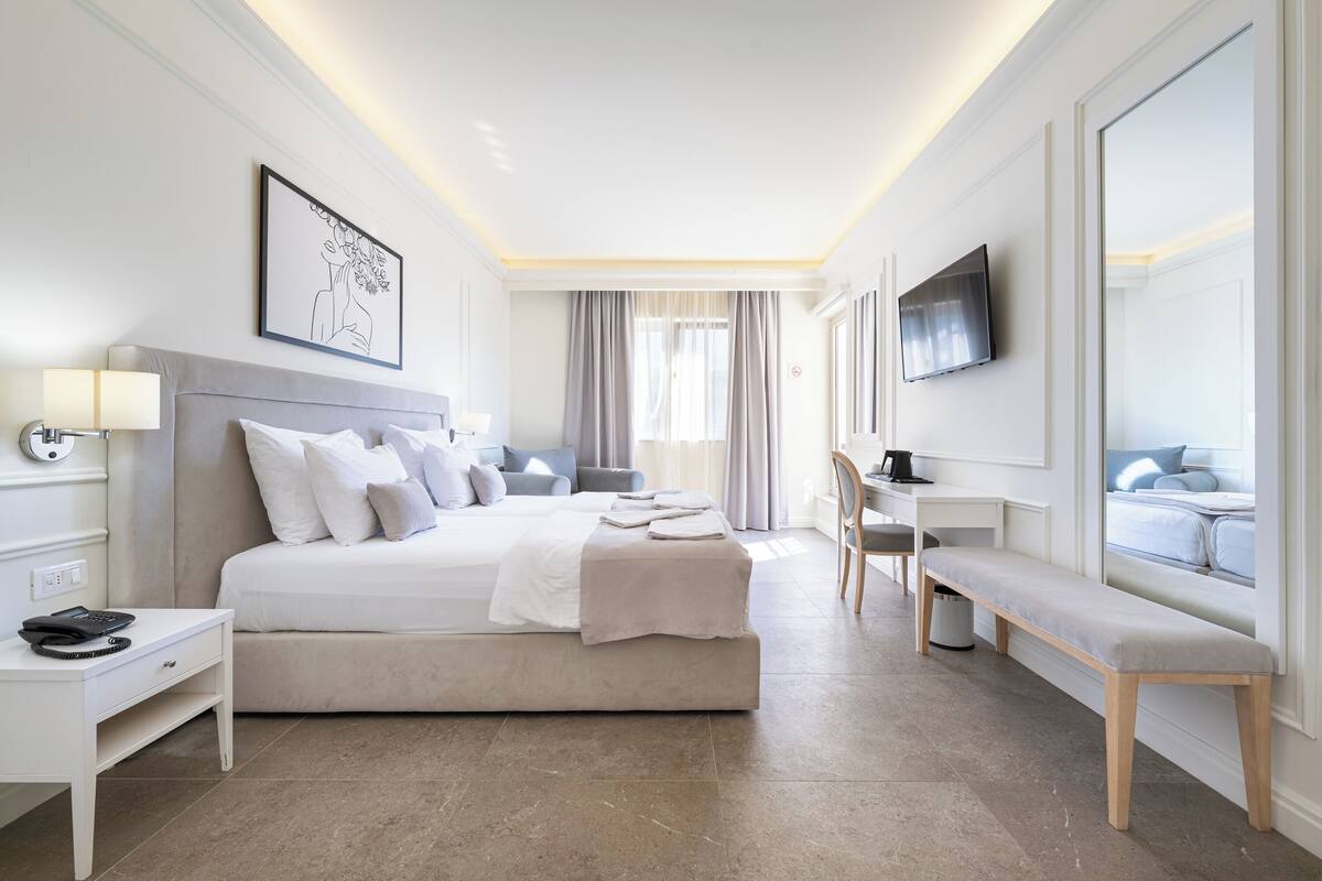 A modern hotel room with a large bed, bedside table, desk, chair, and a TV mounted on the wall.